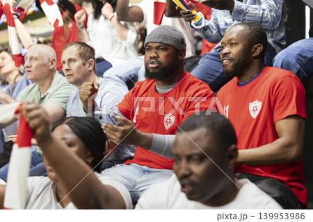 Black soccer fans using mobile sportsbook app during live football match, monitoring live odds and predictions on phone. Crowd of cheering fans, excitement and tension of in-play betting. Black soccer fans using mobile sportsbook app during live football match, monitoring live odds and predictions on phone. Crowd of cheering fans, excitement and tension of in-play betting. 139953986