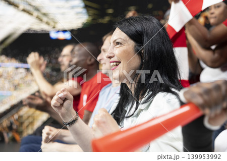 Energetic sports fans reacting to match winner goal during live football game filled with cheering and celebration. Passionate supporters in the stadium express excitement through raised fists. Energetic sports fans reacting to match winner goal during live football game filled with cheering and celebration. Passionate supporters in the stadium express excitement through raised fists. 139953992