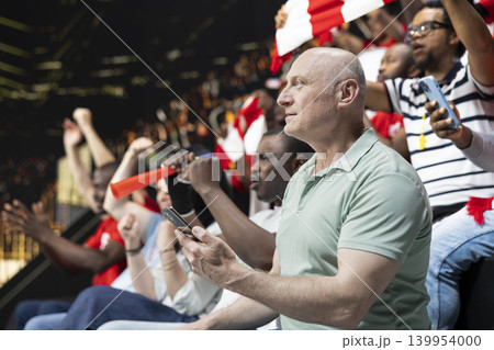 Soccer fan using phone to monitor in-play live betting odds and bet ticket during football match at the stadium. Adult man supporter tracking bet slips and live sportsbook updates. 139954000