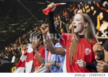 Teenager football fan cheering for the winning team from stadium stands, girl with face paint jumping and screaming after national team wins the world championship. Raised fists and joy. Teenager football fan cheering for the winning team from stadium stands, girl with face paint jumping and screaming after national team wins the world championship. Raised fists and joy. 139954014