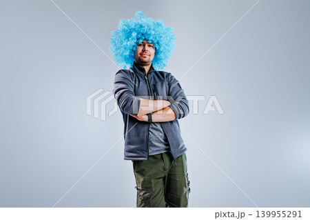 Young man posing in a blue clown wig on gray background Young man posing in a blue clown wig on gray background 139955291