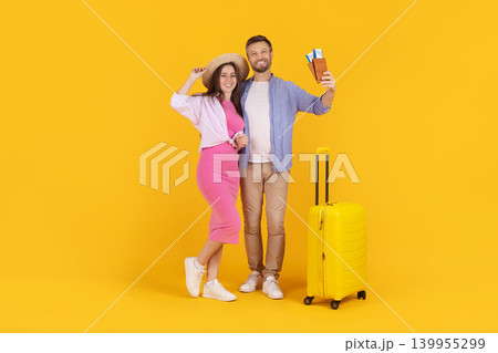 Happy caucasian couple posing with passports and suitcase on yellow studio background Happy caucasian couple posing with passports and suitcase on yellow studio background 139955299