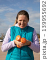 Woman 45 years old holds two orange dumbbells during outdoor sport workout in coastal area on sunny day. Portrait shows effort and exertion during fitness training session outdoors. 139955692