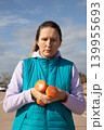 Middle-aged woman holding two orange dumbbells looks focused during outdoor sport workout session in coastal parking lot. Portrait captures concentration during fitness training on sunny day outdoors 139955693