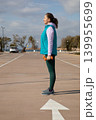 Side view woman standing outdoors holds orange dumbbells during sport workout session in parking lot near sea. Outdoor fitness exercise takes place on sunny day with sea in background. 139955699