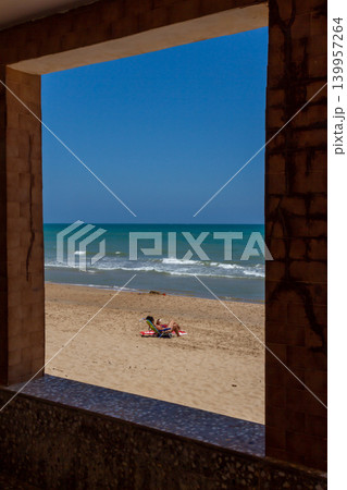 A tourist enjoy a sunny day lying on a towel on a Spanish beach under an umbrella A tourist enjoy a sunny day lying on a towel on a Spanish beach under an umbrella 139957264