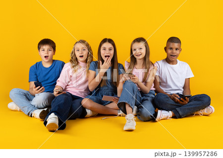Excited group of preteen children sitting with smartphones on yellow studio background Excited group of preteen children sitting with smartphones on yellow studio background 139957286