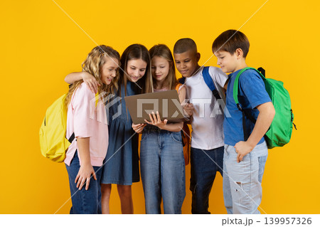 Group of school children gathered around laptop on yellow studio background Group of school children gathered around laptop on yellow studio background 139957326