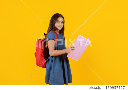 Portrait of schoolgirl with backpack holding notebook on yellow studio background Portrait of schoolgirl with backpack holding notebook on yellow studio background 139957327