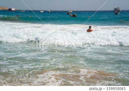 Caucasian man swims in sea waves near boats on the Red Sea coast in Sharm El Sheikh Egypt with turquoise water and summer beach weather. Beach resort lifestyle and seaside tourism on the Red Sea Caucasian man swims in sea waves near boats on the Red Sea coast in Sharm El Sheikh Egypt with turquoise water and summer beach weather. Beach resort lifestyle and seaside tourism on the Red Sea 139958061