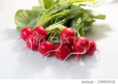 Fresh red radish with green leaves on marble table. Raw organic vegetable as source of fiber and vitamin. Healthy diet, vegan food and nutrition concept. Fresh harvest for cooking salad or raw snack. Fresh red radish with green leaves on marble table. Raw organic vegetable as source of fiber and vitamin. Healthy diet, vegan food and nutrition concept. Fresh harvest for cooking salad or raw snack. 139958418