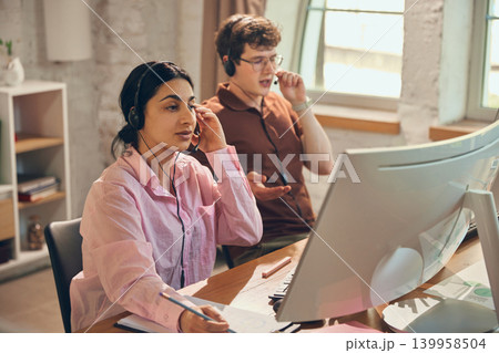 Call center agents handling client calls at computer workstations. 139958504