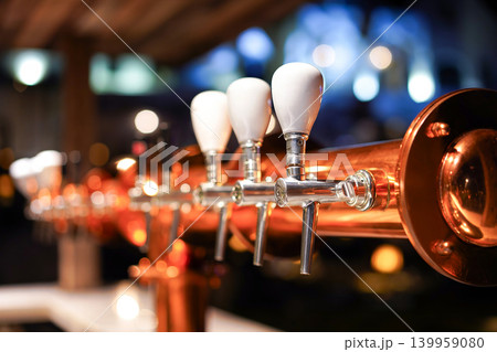 Close-up of polished copper beer taps with soft bokeh lights in a cozy bar setting. Close-up of polished copper beer taps with soft bokeh lights in a cozy bar setting. 139959080