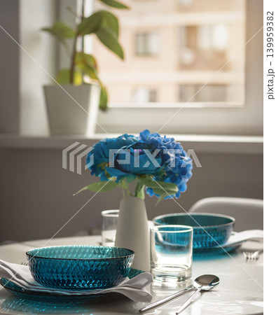 Blue glass tableware on dining table with flowers and soft daylight 139959382