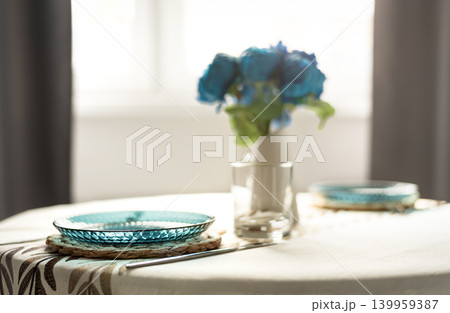 Minimal dining table setting with blue glass plate and flowers in soft sunlight Minimal dining table setting with blue glass plate and flowers in soft sunlight 139959387