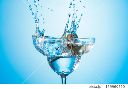 A green olives drops into a martini glass, creating a beautiful splash. 139960220