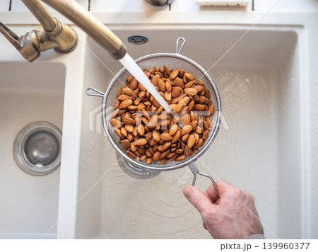Man washes almonds in a metal colander Man washes almonds in a metal colander 139960377