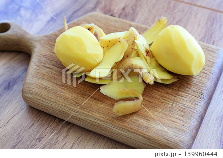 Peeled raw potatoes with brown skin shavings on wooden cutting board, organic cooking ingredients on tabletop backdrop 139960444