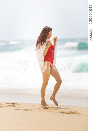 Woman walks on beach in swimsuit while holding a shirt in sunny weather near the ocean in the afternoon 139961045