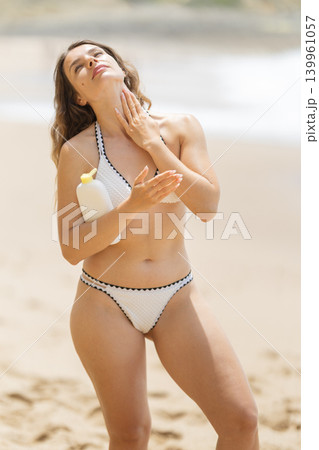 Woman applies sunscreen on the beach near the ocean during a sunny day Woman applies sunscreen on the beach near the ocean during a sunny day 139961057
