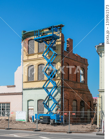 Blue scissor lift beside partially demolished historic brick building during urban redevelopment 139961573