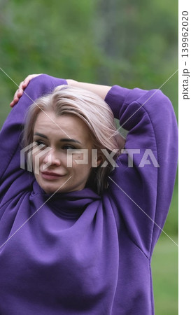 Blonde in purple sweatshirt doing morning exercises, breathing fresh air in forest Blonde in purple sweatshirt doing morning exercises, breathing fresh air in forest 139962020