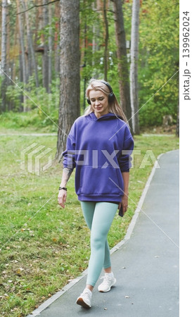 Blonde in purple sweatshirt listening to music on headphones while breathing fresh air in forest Blonde in purple sweatshirt listening to music on headphones while breathing fresh air in forest 139962024