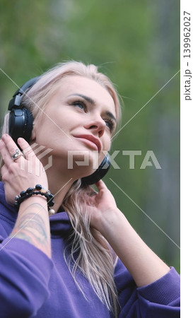 Blonde in purple sweatshirt listening to music on headphones while breathing fresh air in forest Blonde in purple sweatshirt listening to music on headphones while breathing fresh air in forest 139962027