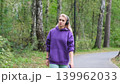 Blonde in purple sweatshirt listening to music on headphones while breathing fresh air in forest 139962033
