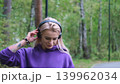 Blonde in purple sweatshirt listening to music on headphones while breathing fresh air in forest 139962034