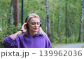 Blonde in purple sweatshirt listening to music on headphones while breathing fresh air in forest 139962036