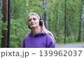 Blonde in purple sweatshirt listening to music on headphones while breathing fresh air in forest 139962037