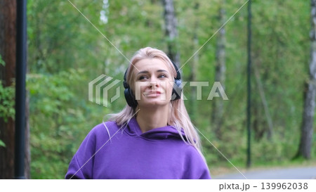 Blonde in purple sweatshirt listening to music on headphones while breathing fresh air in forest 139962038
