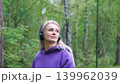 Blonde in purple sweatshirt listening to music on headphones while breathing fresh air in forest 139962039
