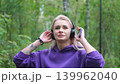 Blonde in purple sweatshirt listening to music on headphones while breathing fresh air in forest 139962040