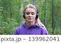 Blonde in purple sweatshirt listening to music on headphones while breathing fresh air in forest 139962041
