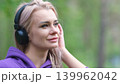 Blonde in purple sweatshirt listening to music on headphones while breathing fresh air in forest 139962042