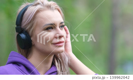 Blonde in purple sweatshirt listening to music on headphones while breathing fresh air in forest Blonde in purple sweatshirt listening to music on headphones while breathing fresh air in forest 139962042