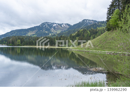 Beautiful landscape of a crystal clear alpine lake with perfect mirror reflection of green pine mountains and dramatic clouds. Silent natural background, Schliersee, Germany Beautiful landscape of a crystal clear alpine lake with perfect mirror reflection of green pine mountains and dramatic clouds. Silent natural background, Schliersee, Germany 139962290