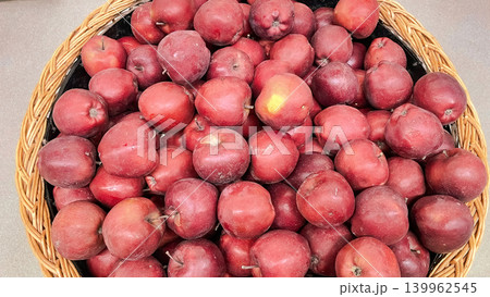 Abundance of fresh ripe red apples displayed in a large wicker basket at a grocery market stall Abundance of fresh ripe red apples displayed in a large wicker basket at a grocery market stall 139962545