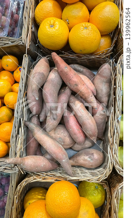 Fresh sweet potatoes and bright oranges displayed in wicker baskets at a grocery store market stall 139962564