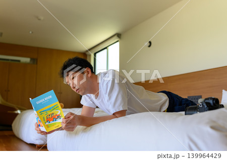 ベッドでガイドブックを読む男性 139964429