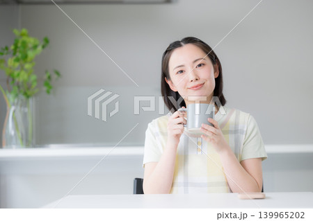 マグカップを持ってコーヒーを飲むくつろぐエプロン姿の主婦のイメージ 139965202