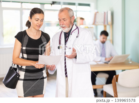 Senior male doctor and woman patient examine papers, discuss medical test. 139965578