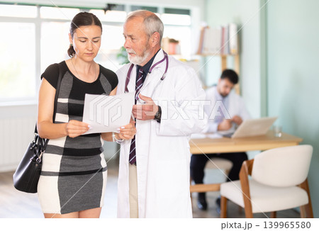 Senior male doctor and sad woman patient examine papers, discuss medical test. Senior male doctor and sad woman patient examine papers, discuss medical test. 139965580