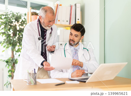 Adult and elderly male doctors working on laptop discussing test results 139965621