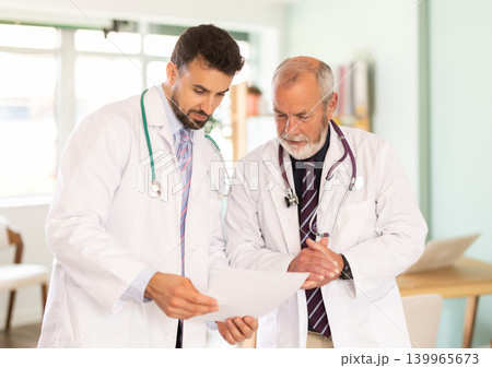 Senior and adult male doctors with documents discuss patients medical history. 139965673