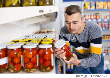 Adult man chooses pickled tomatoes in store Adult man chooses pickled tomatoes in store 139965675