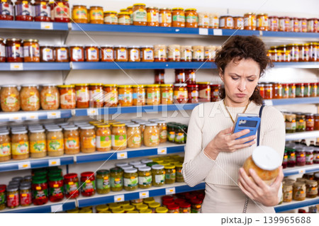 Female shopper scans barcode on jar of sauerkraut using a smartphone while shopping in grocery store 139965688