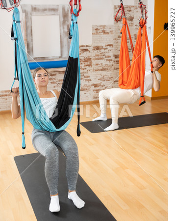 Girl doing aerial pilates exercises with suspended hammock in studio Girl doing aerial pilates exercises with suspended hammock in studio 139965727